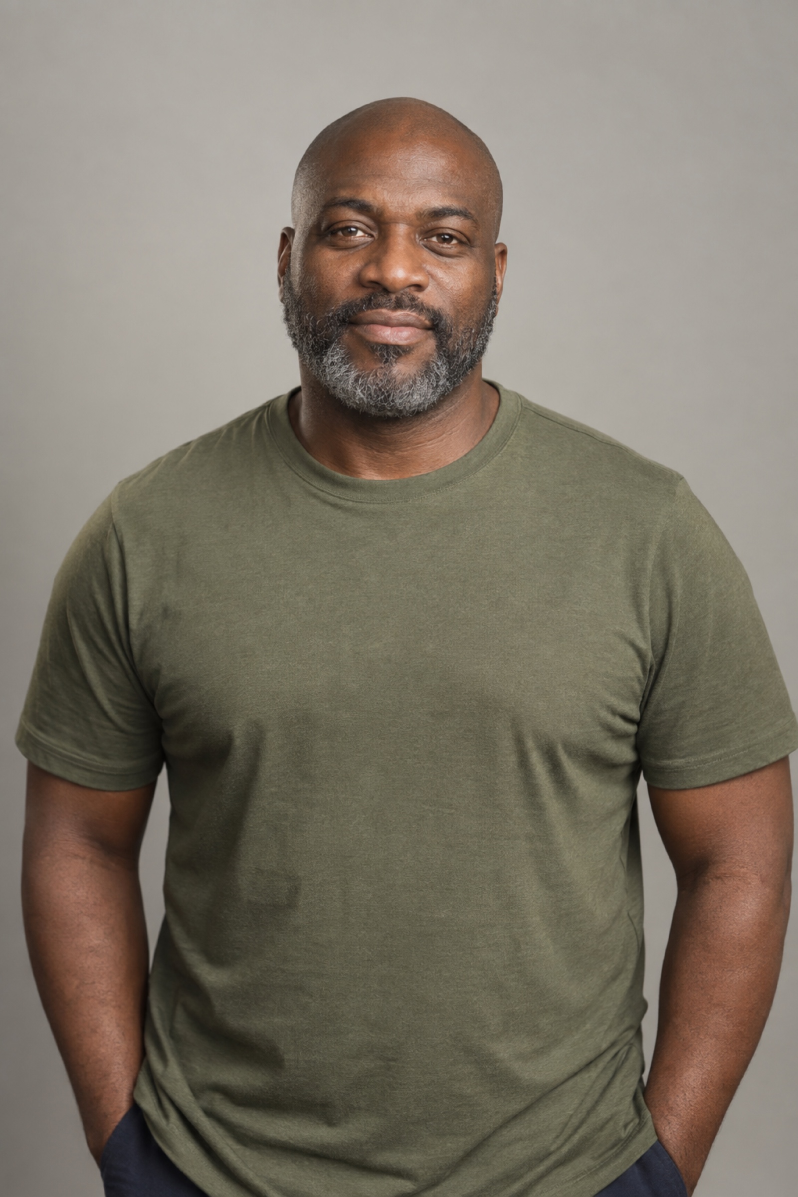 Studio portrait of a man in their 40s with shaved head, wearing an olive shirt, against a warm grey background.