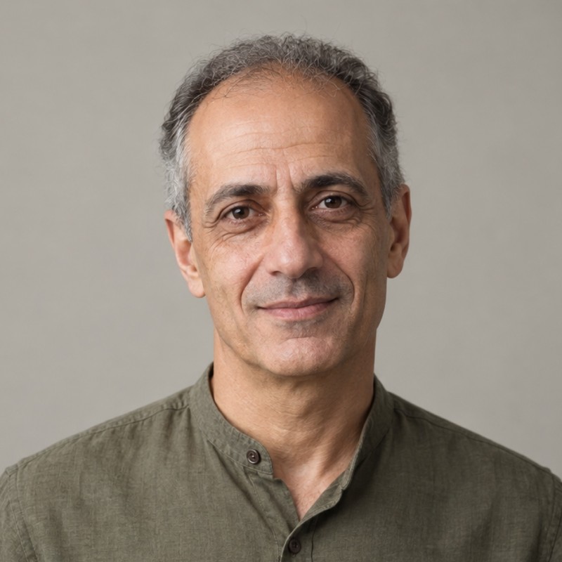 Head and shoulders of a man in their 50s with receding short salt-and-pepper hair, wearing an olive shirt, against a warm grey background.